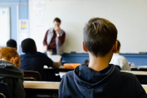 Boy in black hoodie sitting at a desk in a classroom.