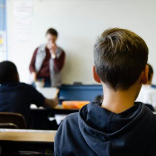 Boy in black hoodie sitting at a desk in a classroom.